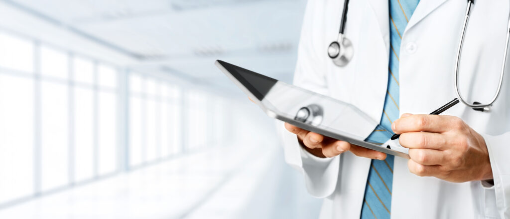 A doctor in a lab coat uses a tablet to take notes in a modern healthcare setting, emphasizing digital technology in medical practices.