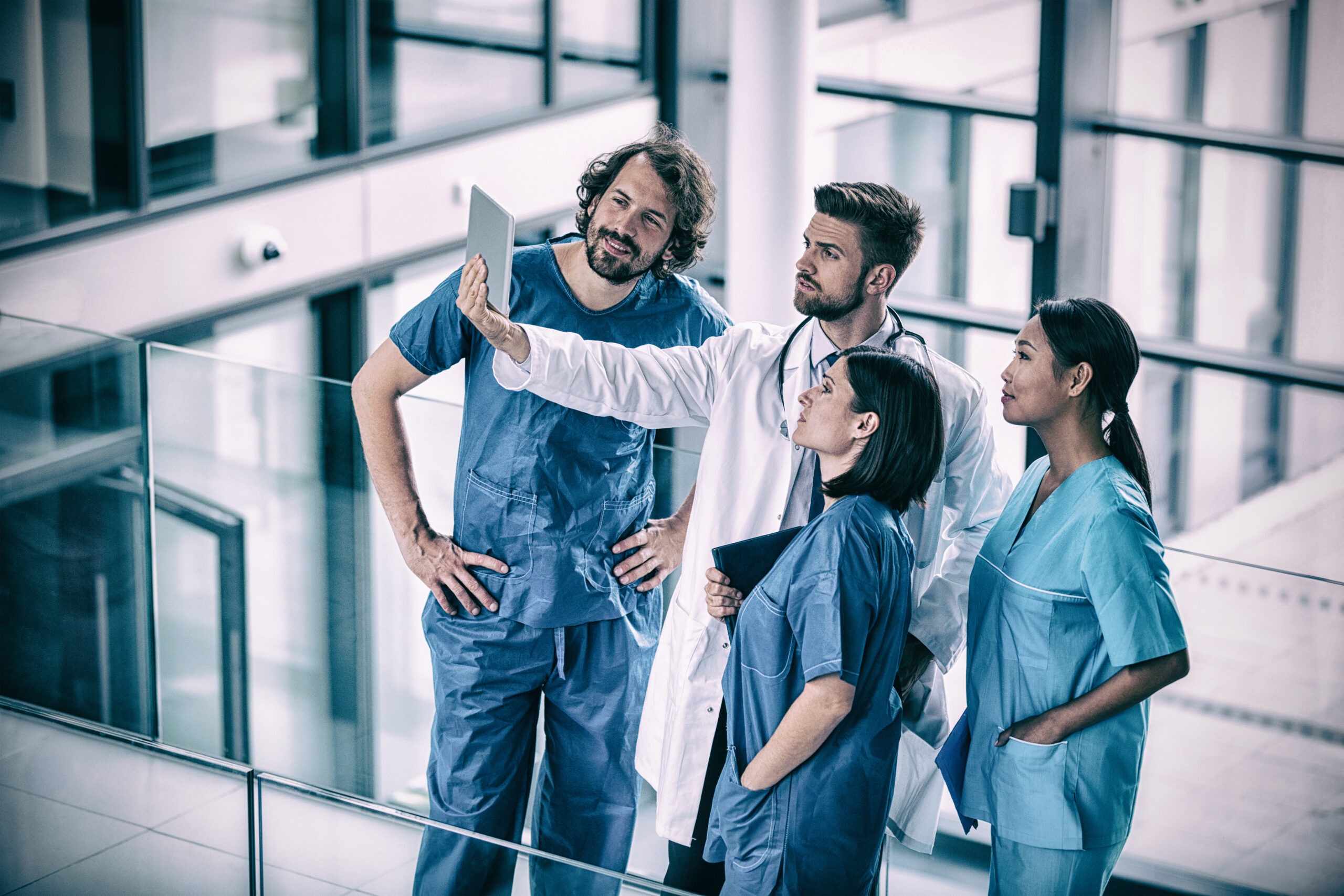Healthcare professionals discuss patient information on a tablet in a modern hospital setting, emphasizing teamwork and technology in medical care.